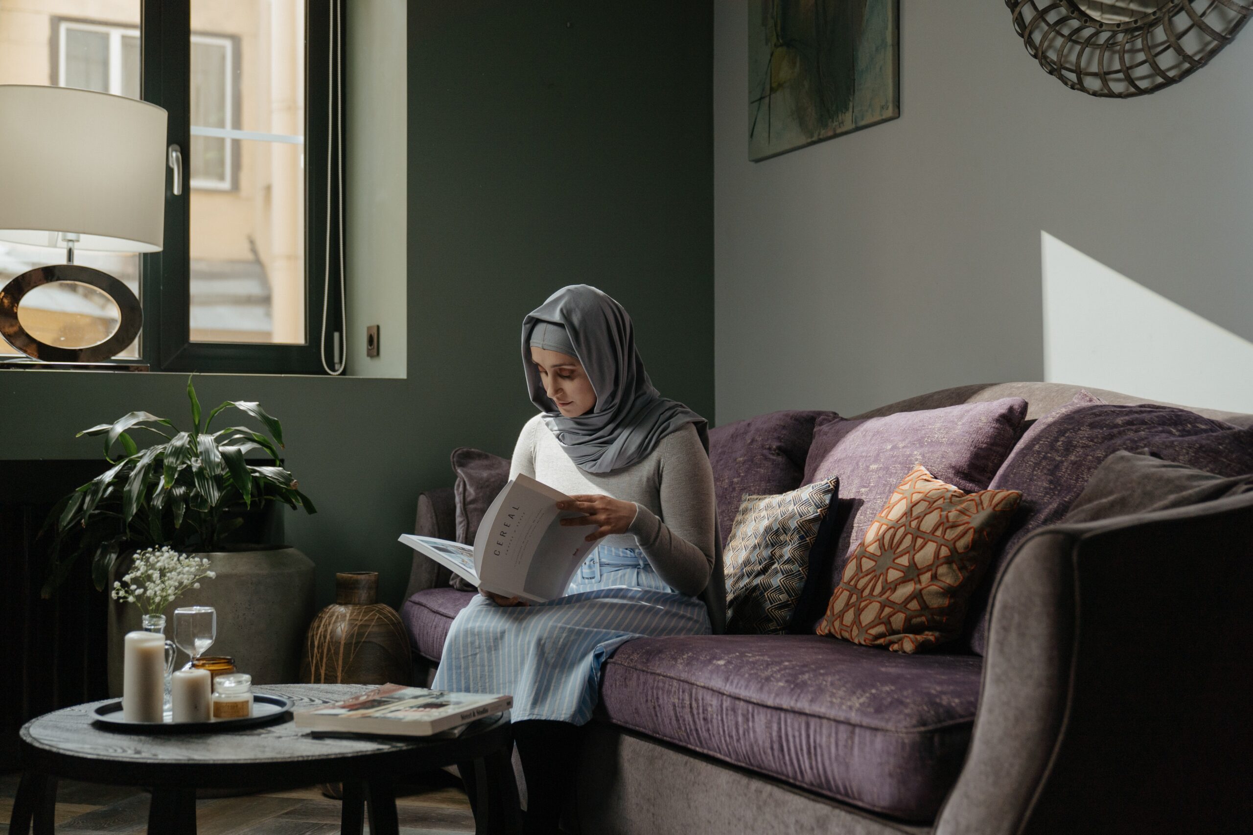 En kvinna i slöja som sitter i en soffa och läser en bok i en hemmamiljö.